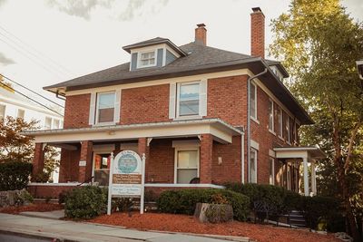Historic two-story brick building with a welcoming porch and greenery.