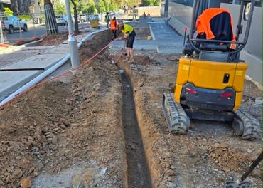Workers digging a trench next to a small excavator on a construction site.