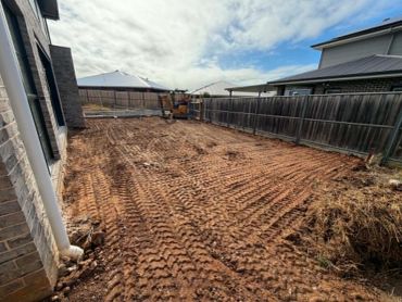 Cleared backyard with fresh soil and visible tire tracks under a partly cloudy sky.