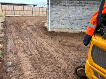 Freshly leveled dirt beside a brick house with tractor tire marks.