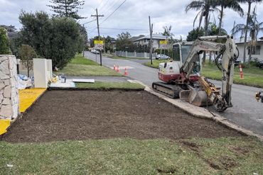 A freshly dug patch of soil beside a street with a mini excavator.