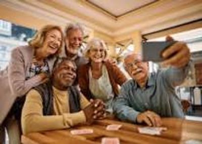 A group of elderly friends taking a selfie while playing cards.