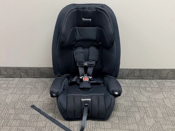 Black Harmony child car seat with safety harness on carpet.