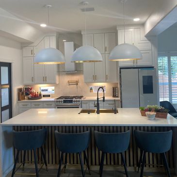 Modern kitchen with white cabinetry, large island, and black bar stools under pendant lights.