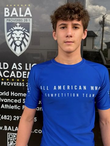 Teen boy wearing a blue All American MMA shirt in front of a Bala Academy sign.