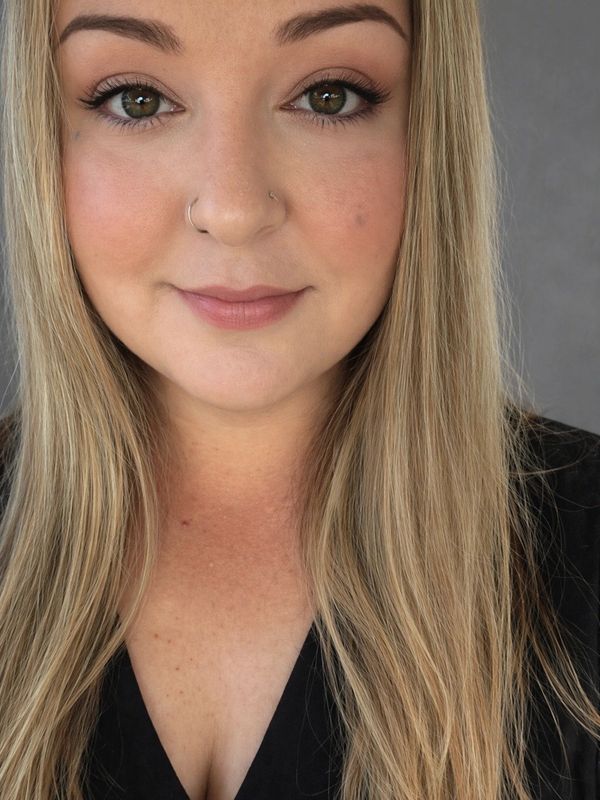 Close-up portrait of a smiling woman with long blonde hair and nose rings.