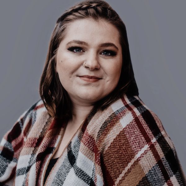 Woman with braided hair wrapped in a cozy plaid shawl, smiling gently.