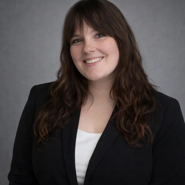 Smiling woman with long brown hair in black blazer and white top.