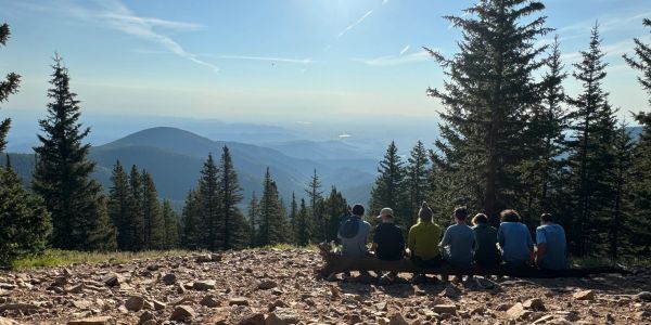 Group of people sitting on a log enjoying mountain view.