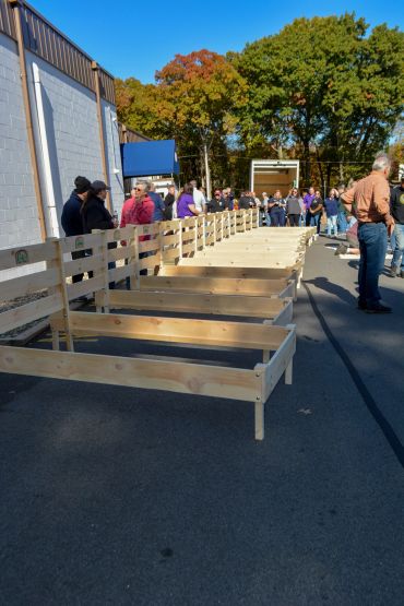 People inspecting wooden bed frames outdoors on a sunny day.