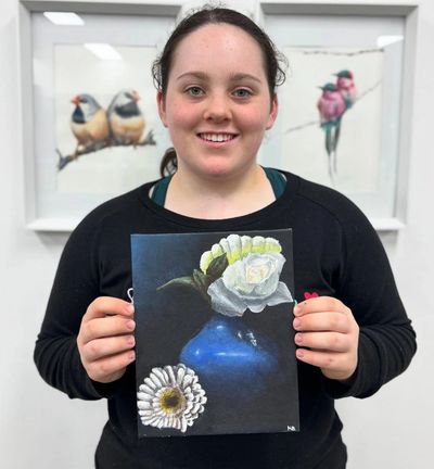 Young woman proudly holding a floral painting with birds artwork in the background.