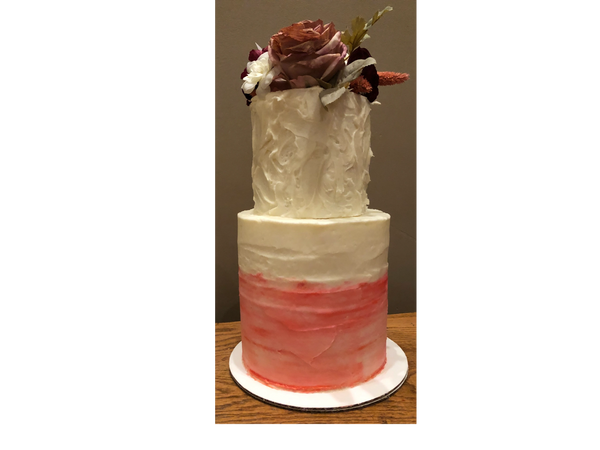 Two tiered tall cake, with flowers as the topper, rough iced  with white icing and pink icing 