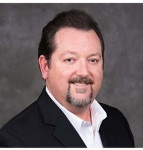 Professional man in a black suit smiling against a gray background.