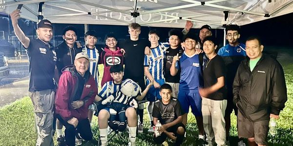 Youth soccer team posing together under a tent at night.