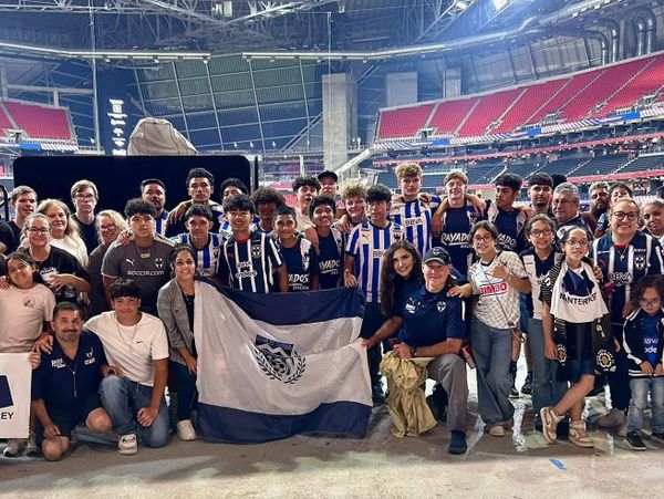 Group photo of a soccer team and supporters holding a team flag in a stadium.