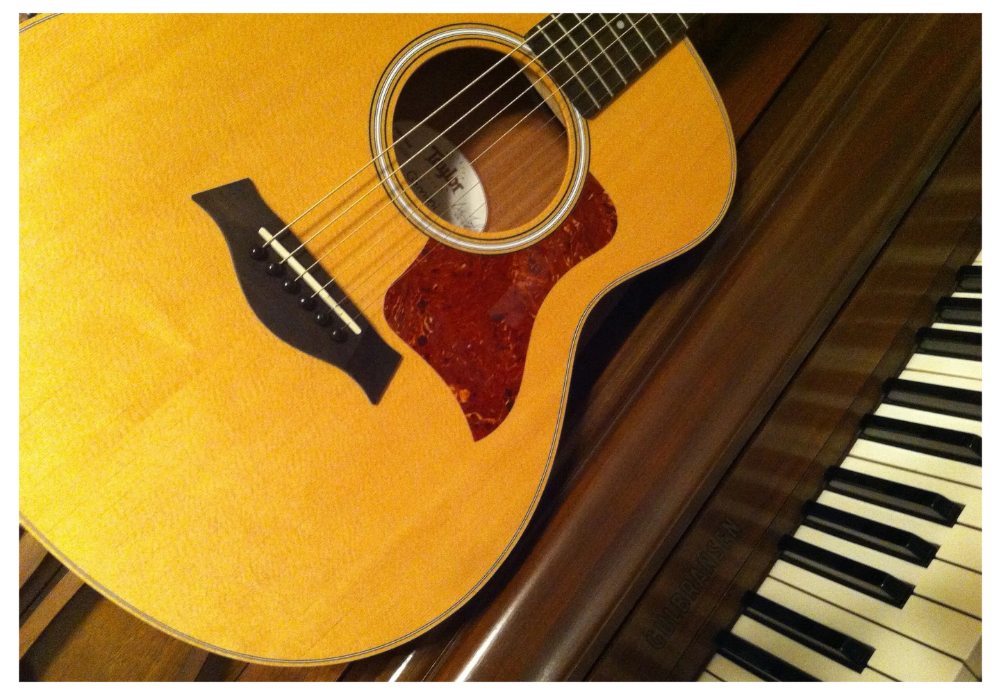 Acoustic guitar resting against an upright piano, with the piano keys visible