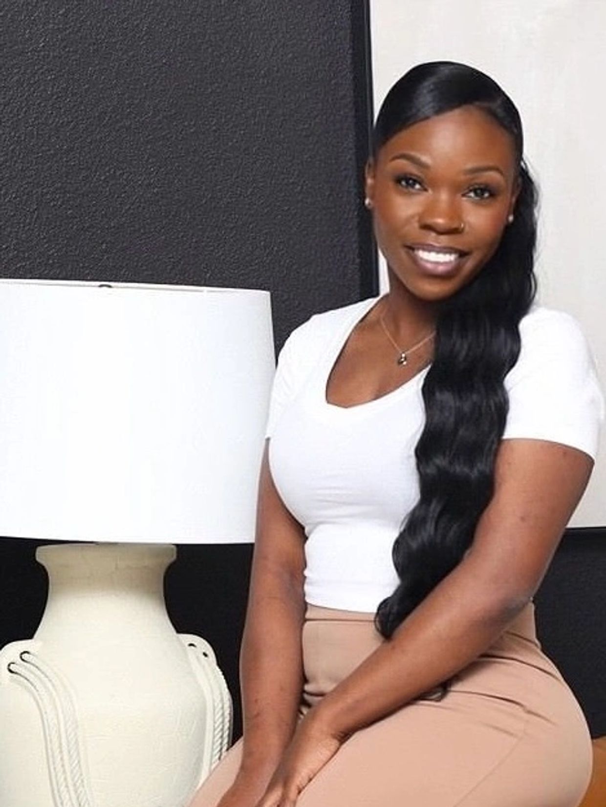 Woman with long wavy hair sitting on a mustard chair next to a white lamp.
