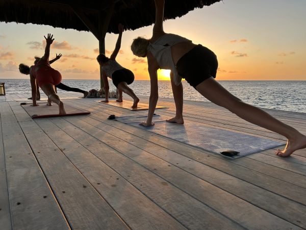 People doing yoga on wooden deck at sunset by the sea.