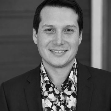 Portrait of a smiling man in a suit with a patterned shirt.
