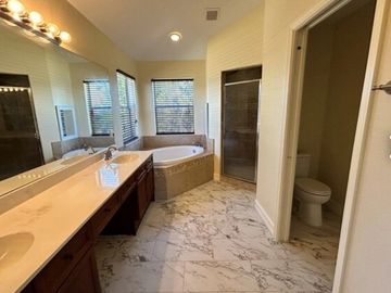 Spacious bathroom with double sinks, a corner bathtub, and separate shower and toilet areas.