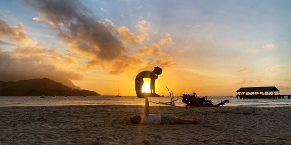 Two people practicing acro yoga on a beach at sunset.