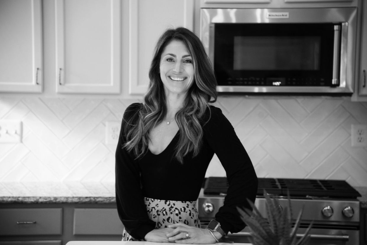 Smiling woman standing in a modern kitchen with arms rested on the counter.