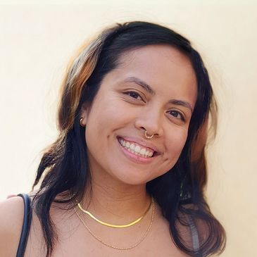 Young woman smiling with nose ring and layered necklaces.