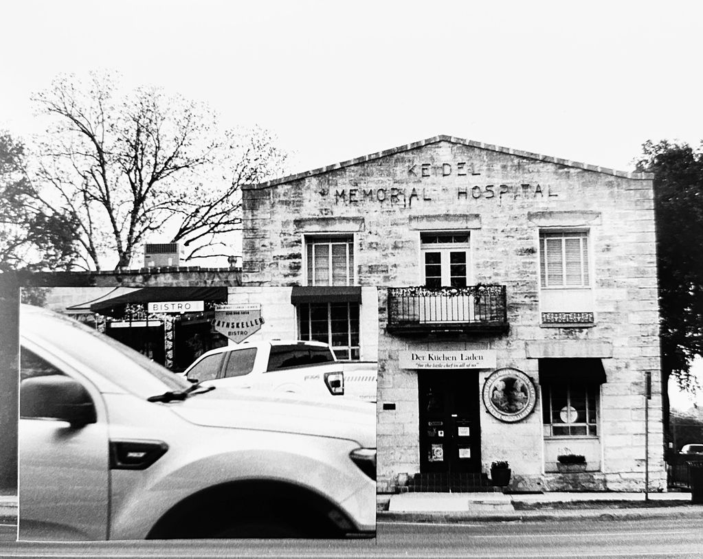 Black and white image of an old stone building with cars in front.