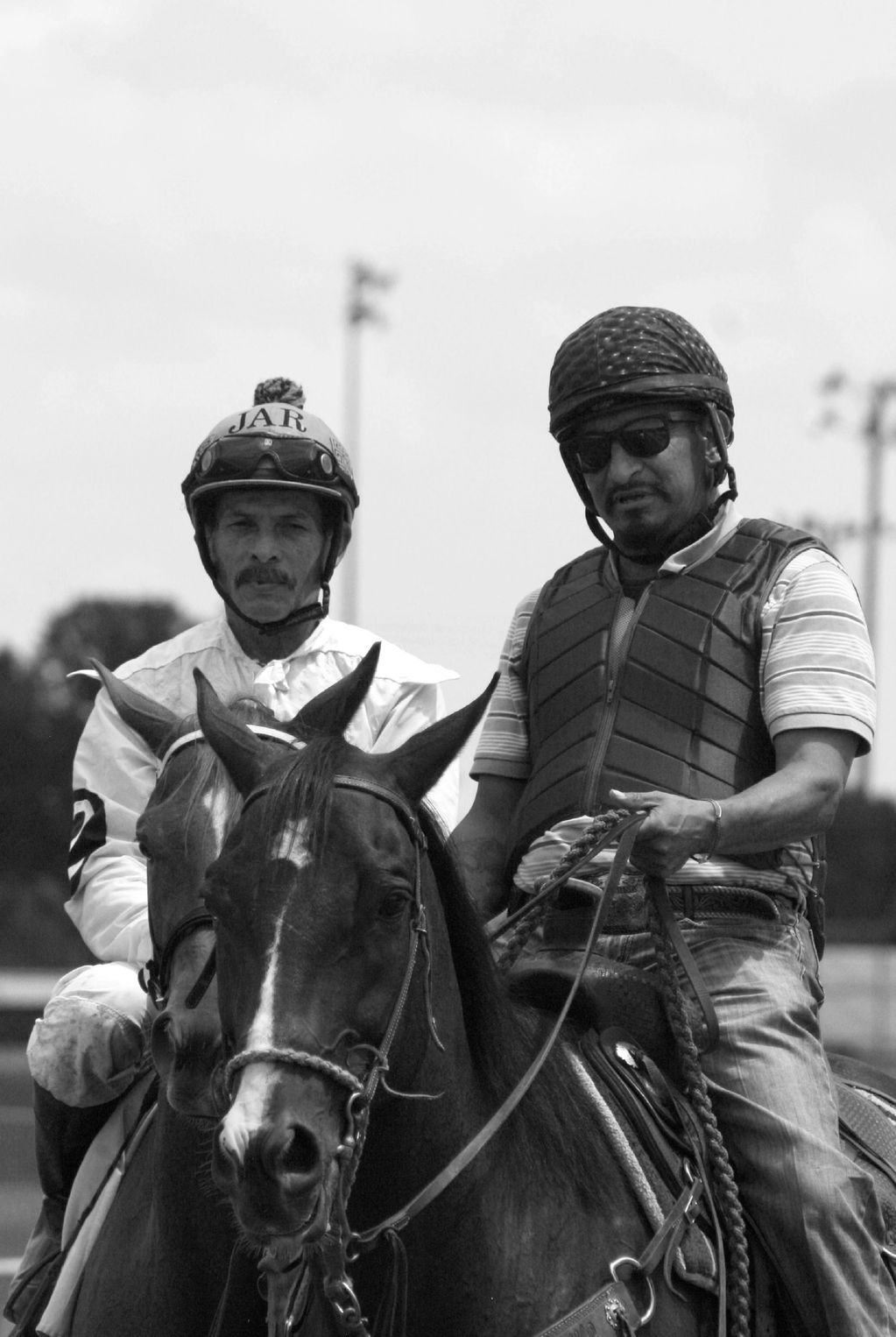 Two men on horseback, one in racing gear, one in casual wear.