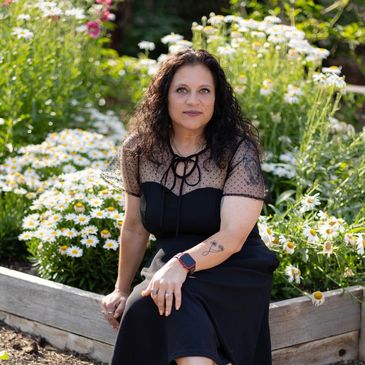 Woman in a black dress sitting by a flower bed with daisies.