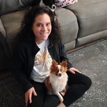 A woman sitting on the floor with a small dog on her lap and another dog on the couch.