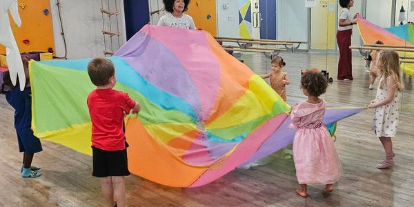 Children play with a colorful parachute in a gym under adult supervision.