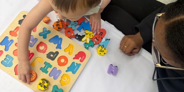 Child playing with alphabet puzzle alongside an adult.