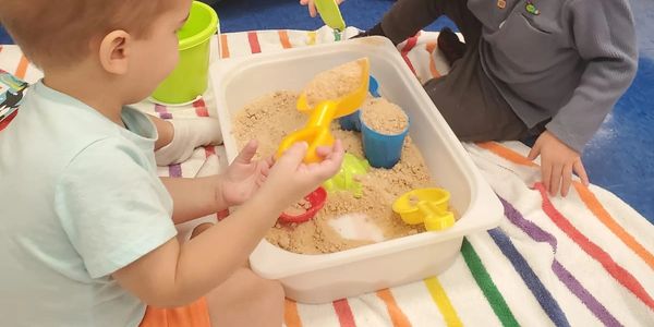Two toddlers playing with sand toys in a sensory bin.