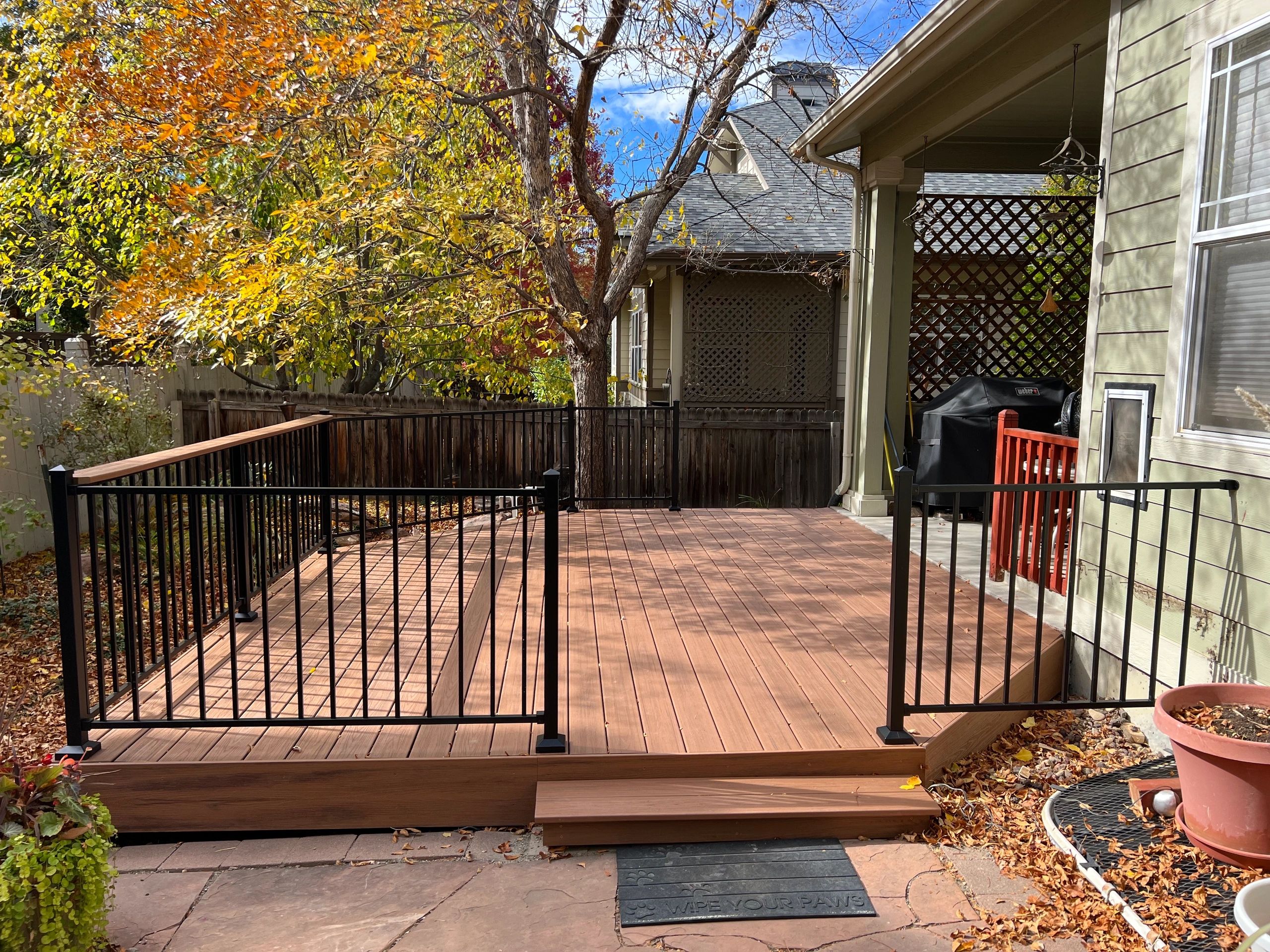 Wooden deck with black metal railing and autumn trees in the background.
