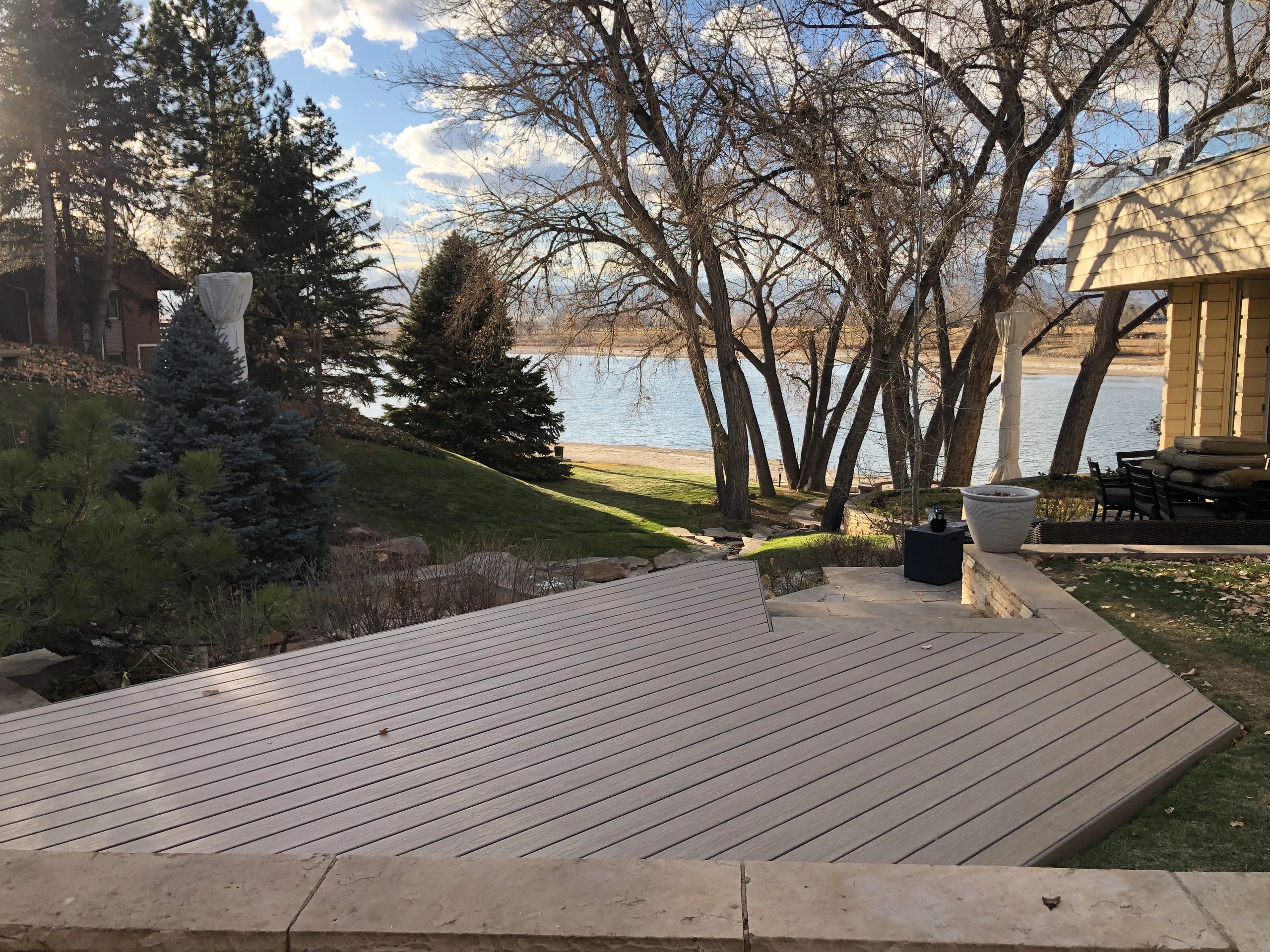 Backyard with trees overlooking a calm lake under a partly cloudy sky.