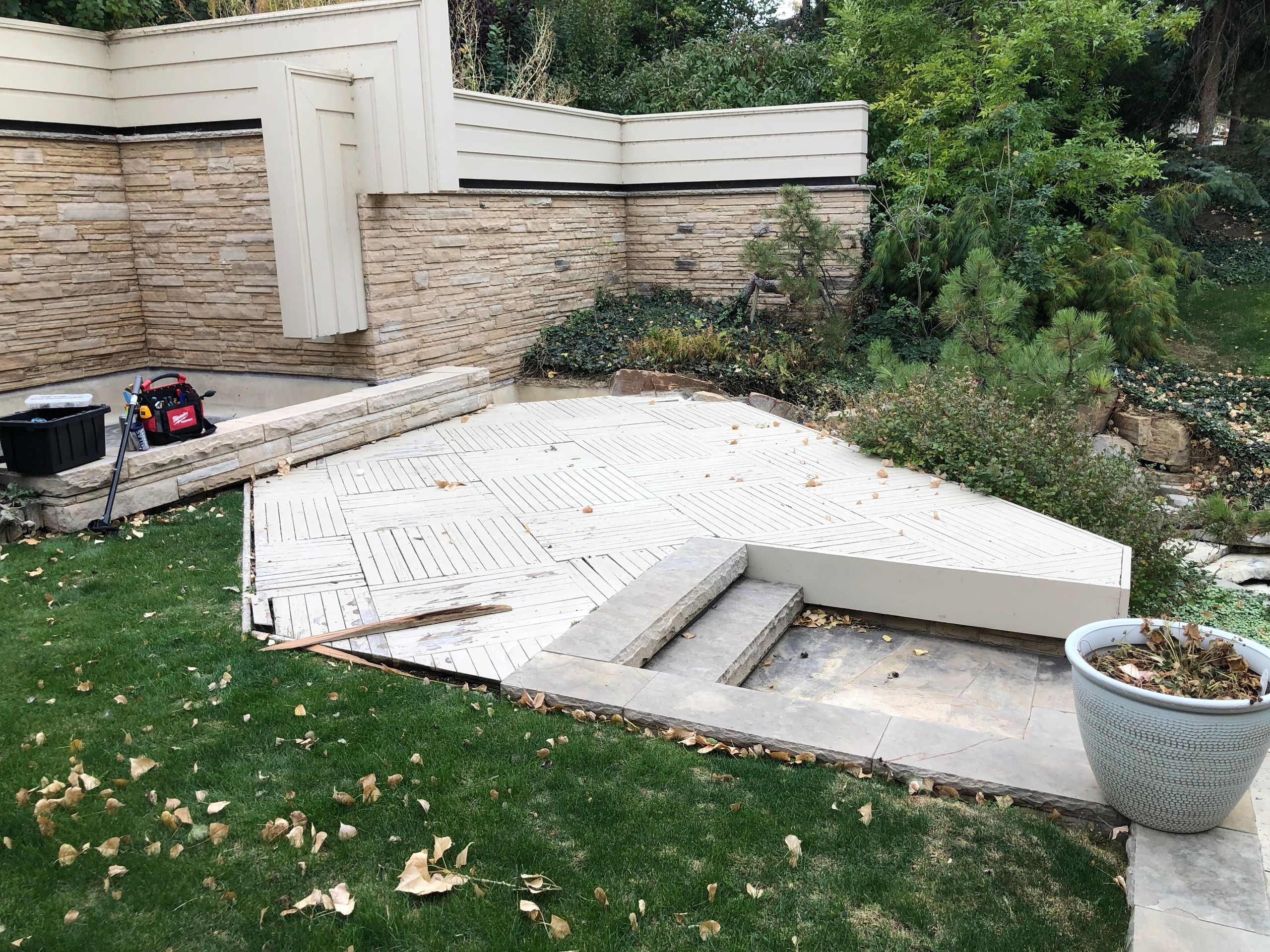 Backyard patio with stone walls, tools, and greenery.