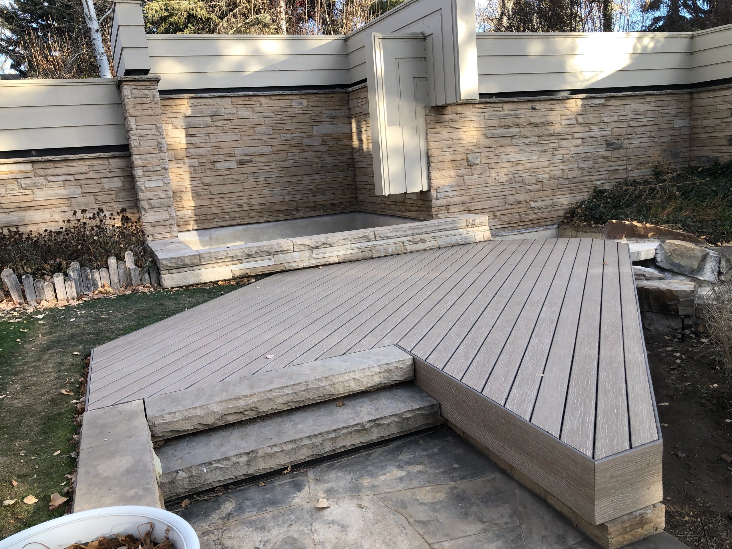 A backyard patio with stone walls and a wooden deck area.