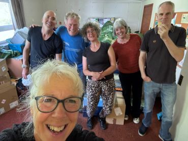 Group selfie of six friends in a room with boxes.