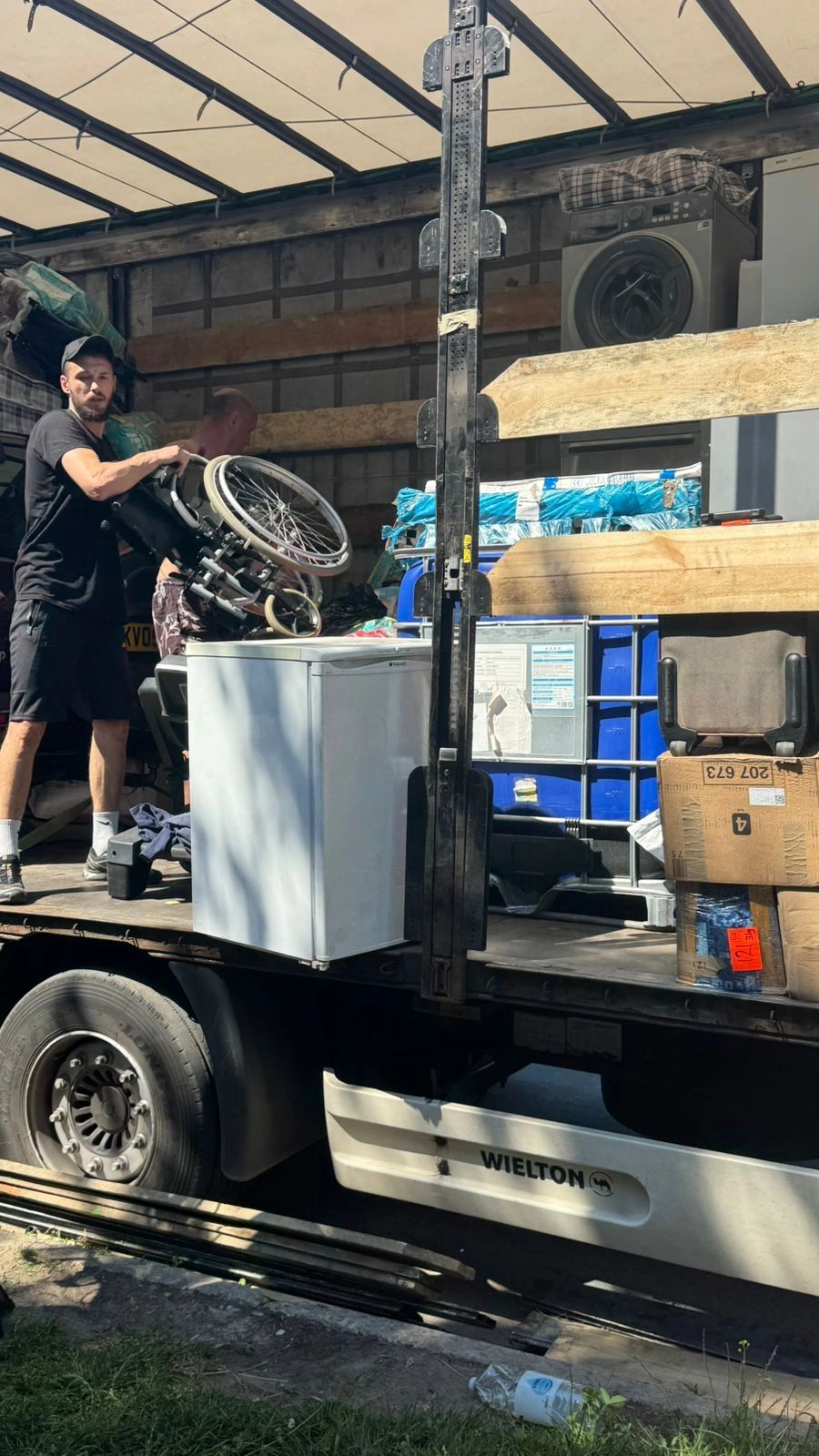 Man loading wheelchair onto truck with various items.