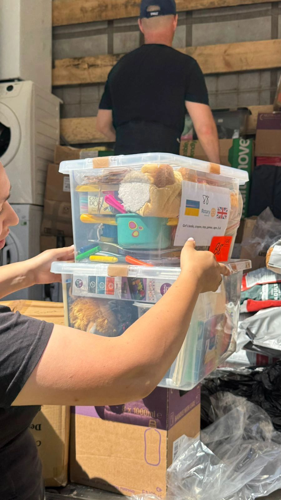 Person holding clear plastic bins filled with toys and books.