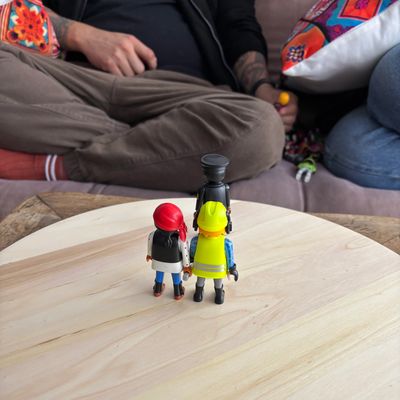 Figuras de juguete sobre una mesa, personas al fondo desenfocadas.