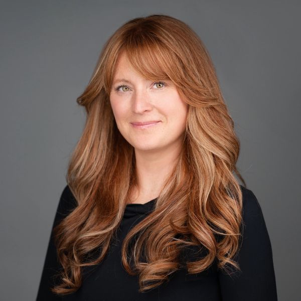 Smiling woman with long wavy red hair against a gray background.