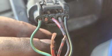 Close-up of hand holding a damaged electrical connector with exposed wires.