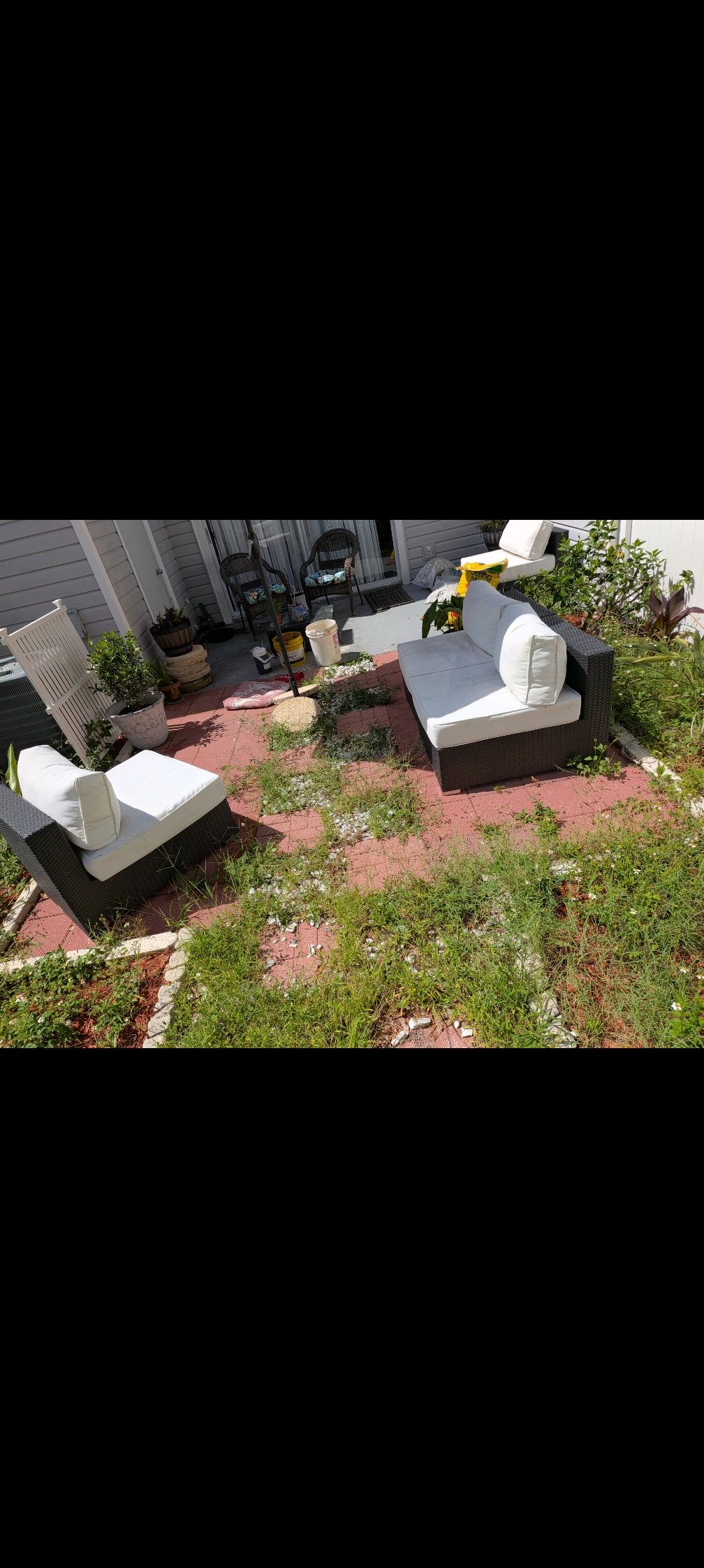 Outdoor patio with furniture and overgrown weeds.