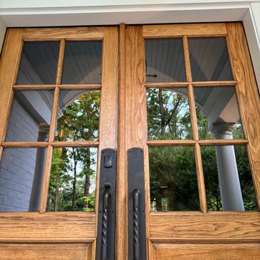 Wooden double doors with glass panes reflecting trees and a white porch.