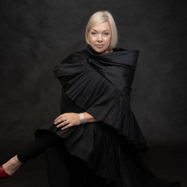 Elegant woman in a dramatic black ruffled outfit against a dark background.