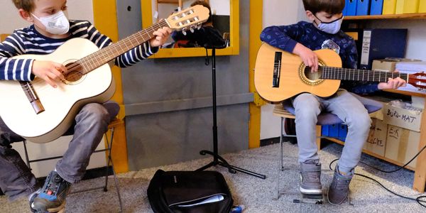 Zwei Jungen mit Corona-Schutzmasken beim Gitarrenunterricht