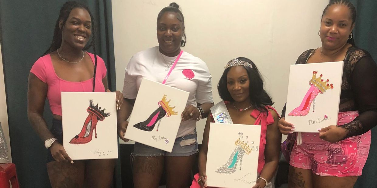 Four women proudly holding paintings of high-heeled shoes with crowns.