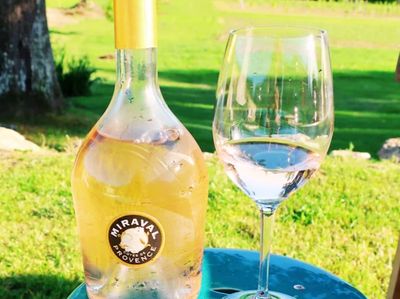 Chilled Miraval rosé wine bottle with a glass on a blue table outdoors.